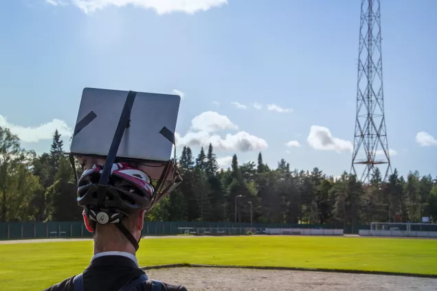A man with a helmet-laptop construction on his head looks out into the landscape. Photo.