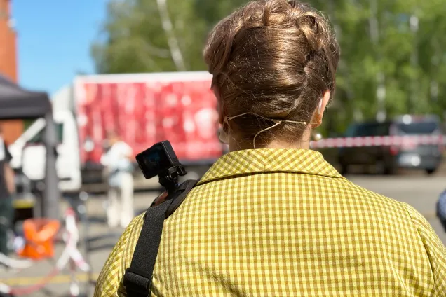 Woman from behind with small camera and headset. Photo.