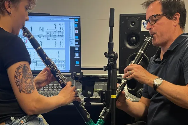 Two musicians, each with a clarinet, facing each other. Photo.